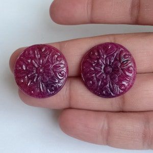 Può includere: Due cabochon rotondi in rubino intagliati con un motivo floreale. I cabochon sono di un colore rosa intenso con una sfumatura viola.