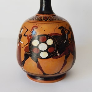 May include: A black and orange ancient Greek pottery vase with a black handle and a scene of warriors painted on the side. The vase has a round body and a narrow neck. The scene depicts two warriors in combat, one with a shield and the other with a spear. The vase is decorated with geometric patterns and the inscription "AXILEO".