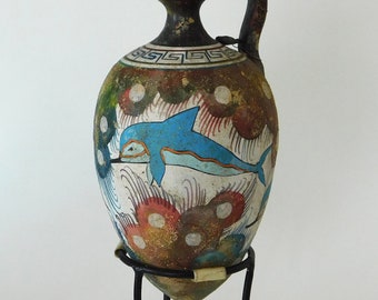 May include: A ceramic amphora with a blue dolphin painted on it. The amphora is decorated with a geometric pattern and white dots. It is on a black metal stand.