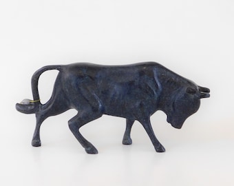 May include: A dark blue bull figurine with a curved tail and horns. The sculpture is made of a solid material and stands on four legs. The bull is a decorative item.