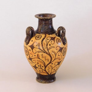 May include: A small, antique-style vase with two handles. The vase has a light tan background with dark brown floral and vine patterns. The rim and base are dark brown, and the handles are curved.