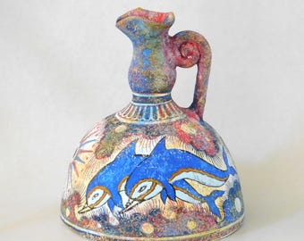 Pode incluir: Jarro de cerâmica pintado à mão com um design de golfinhos azuis e brancos. O jarro tem uma alça e um bico, com um acabamento colorido e texturizado. A base é redonda e o design lembra a cerâmica antiga.