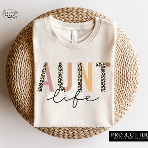 May include: A white t-shirt with the text "AUNT life" in pink, orange, and yellow letters with a leopard print pattern. The letters are outlined in black.