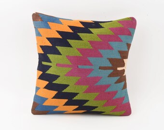 May include: A colorful throw pillow with a geometric pattern in shades of blue, green, orange, pink, and brown. The pillow is made of woven fabric and has a square shape.