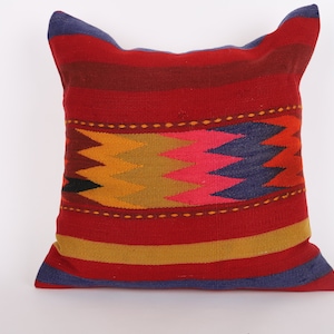 Puede incluir: Una almohada de rayas rojas, azules, amarillas y naranjas con un patrón geométrico en el centro.