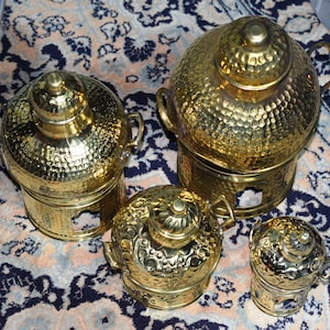 Puede incluir: Cuatro platos de servir de metal dorado con tapas. Los platos están decorados con una textura martillada y tienen forma redonda. Los platos están dispuestos sobre una alfombra estampada.