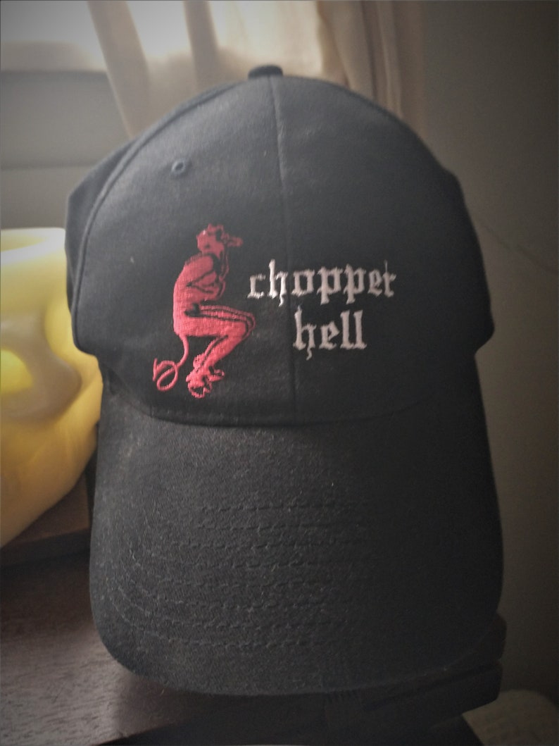 Puede incluir: Gorra de b&eacute;isbol negra con visera curva. La gorra presenta un diablo rojo bordado y las palabras "chopper hell" en letras g&oacute;ticas blancas. La gorra est&aacute; hecha de tela texturizada.