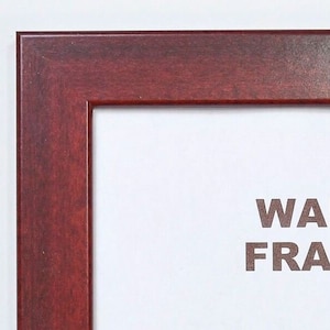 May include: A dark red wood picture frame with the text "WALL FRAME" and "WEST COAST FRAMES LLC" in white lettering. The text "PORTLAND, OREGON" is also included in white lettering.