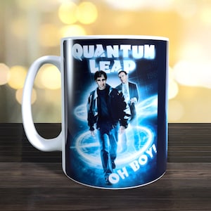 Könnte beinhalten: Weiße Keramiktasse mit einem blauen und schwarzen Bild von zwei Männern aus der Fernsehserie "Quantum Leap". Das Bild enthält den Titel der Serie und den Text "Oh Boy!"
