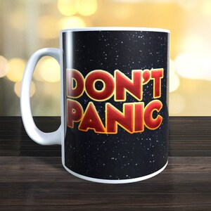 May include: White ceramic mug with a black background and the words "Don't Panic" in red and yellow lettering.