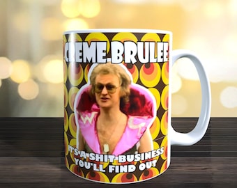 May include: White ceramic mug with a colorful retro design featuring a man wearing sunglasses and a pink jacket. The text "CREME BRULEE IT'S A SHIT BUSINESS YOU'LL FIND OUT" is printed on the mug.