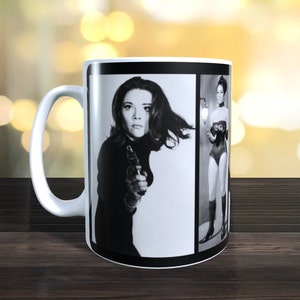 May include: A white ceramic mug with a black and white photo of a woman holding a gun. The photo is split into two sections, with the woman on the left and a different photo of the same woman on the right.
