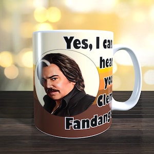 May include: White ceramic mug with a brown, orange, and yellow background. The mug features a cartoon illustration of a man with a mustache and the text "Yes, I can hear you Clem Fandango".