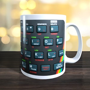 May include: White ceramic mug with a black and white image of a vintage computer keyboard. The keys have labels like "Graphics", "Black", "Delete", "Point", "Code", "Peek", "Tab", "Input", "Poke", "Print", "Len", "List", "Screens", "Symbol Shift", "Break", and "Space".