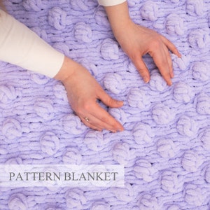 Puede incluir: Primer plano de una suave manta de color lavanda con un patrón texturizado y abultado. La manta está hecha con un hilo grueso y tiene una textura suave y peluda. El texto "PATTERN BLANKET" es visible en la parte inferior de la imagen.