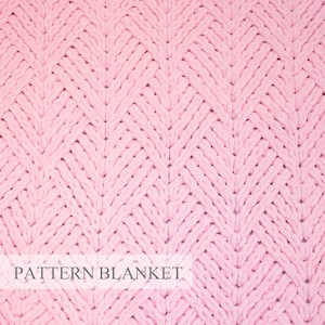 May include: A soft, light pink knitted blanket featuring a repeating chevron or diamond-shaped texture pattern. The textile has a thick, chunky yarn construction with visible loops. A white rectangular overlay displays the text PATTERN BLANKET.