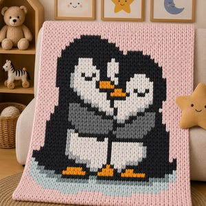 May include: A chunky knit blanket in a soft pink hue featuring a large, central graphic of two penguins embracing. The penguins are rendered in black, white, and grey yarn with orange beaks and feet, standing on a light blue icy patch.