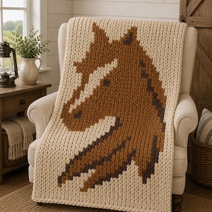 May include: A chunky knit throw blanket featuring a large, pixelated horse head design in shades of brown and dark brown against a cream-colored background. The blanket is draped over a chair, showcasing the thick, textured yarn stitches throughout.