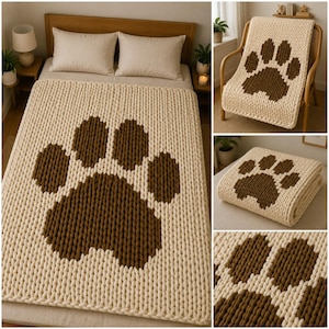 May include: A cream-colored, chunky knit blanket with a large brown paw print design. The blanket is displayed on a bed and draped over a chair, showcasing its texture and pattern. The cozy, oversized throw is perfect for snuggling.