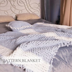 May include: A grey and white striped chunky knit blanket with a fluffy texture. The blanket is draped over a bed with pillows.