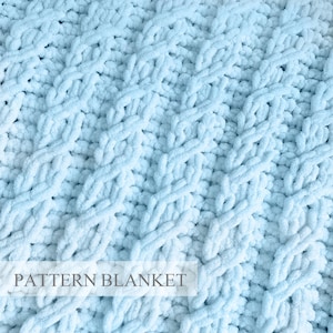 May include: A light blue knitted blanket featuring a textured cable stitch pattern throughout the fabric. The surface displays a repeating design of vertical braided cables separated by rows of knit stitches. The text PATTERN BLANKET is visible.