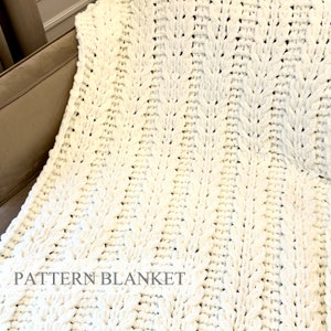 May include: A white chunky knit blanket featuring a repeating vertical cable stitch pattern. The soft, textured yarn creates a thick, plush appearance throughout the entire surface. The text PATTERN BLANKET is printed in a simple gray font at the bottom.