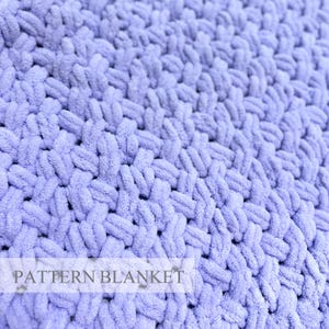 May include: A light purple blanket featuring a thick, chunky knit texture with interlocking loops. The surface has a soft, fuzzy appearance created by the yarn construction. The text "PATTERN BLANKET" is printed in a simple font across the lower section.