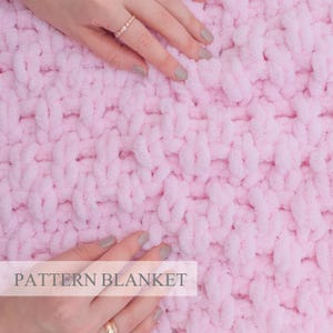 May include: A close-up of a pink knitted blanket with a textured pattern. The blanket is soft and fluffy, and it is perfect for cuddling up on the couch.