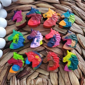 May include: Twelve colorful unicorn-shaped crayons arranged in a circle on a woven basket surface. The crayons are made of a blend of colors, including red, blue, green, yellow, and purple.