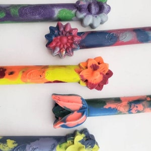 May include: Five colorful crayons with flower-shaped tops. The crayons are made by Crayola and have a variety of colors and patterns.