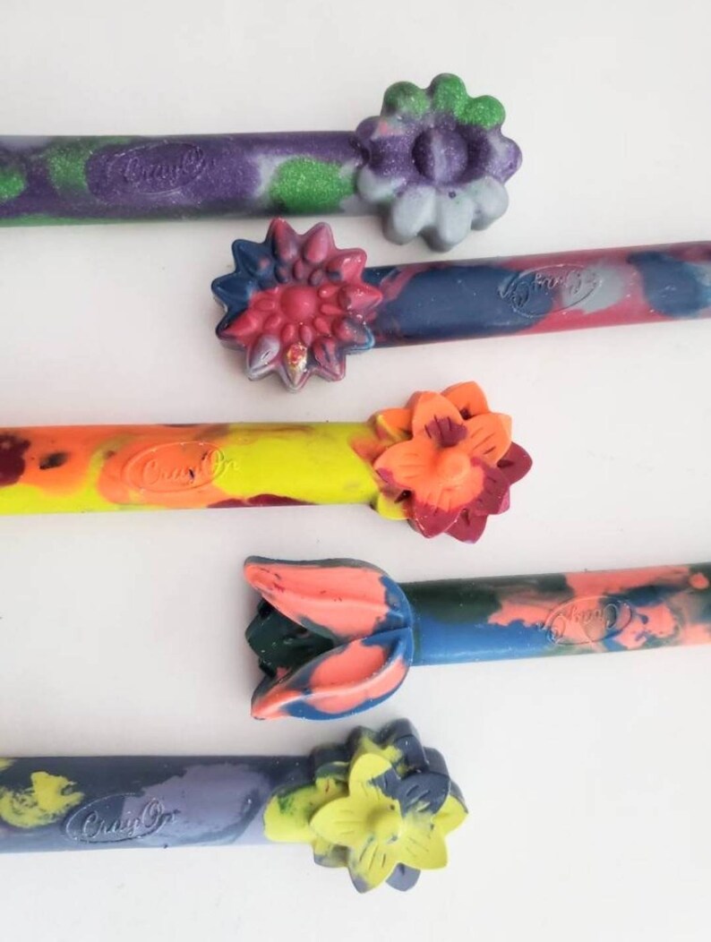 May include: Five colorful crayons with flower-shaped tops. The crayons are made by Crayola and have a variety of colors and patterns.