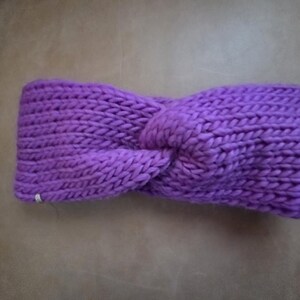 May include: A vibrant purple knitted headband with a twisted knot design. The headband is made of thick, textured yarn, and is designed to keep the ears warm. The accessory is a stylish addition to any cold-weather outfit.