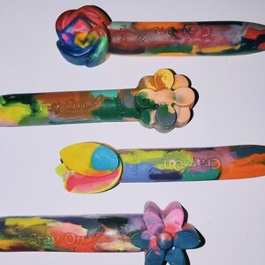 May include: Four Crayola Crayon On brand crayons with different flower-shaped ends. The crayons are multi-colored and have the text "Cray On" printed on them.