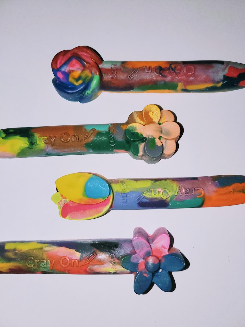 May include: Four Crayola Crayon On brand crayons with different flower-shaped ends. The crayons are multi-colored and have the text "Cray On" printed on them.