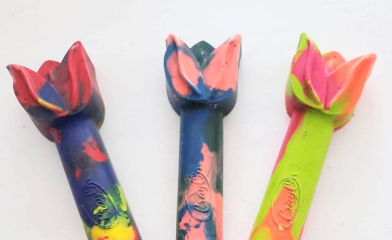May include: Three colorful crayon shaped like tulips. The crayons are blue, green, and orange with red, pink, and yellow accents. The crayons are labeled "Crayola".