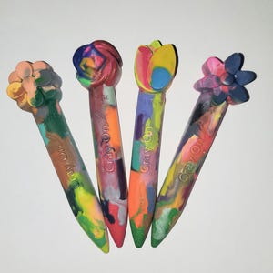 May include: Four colorful crayons shaped like flowers. The crayons are labeled "Crayon On!" and feature a variety of colors and designs.