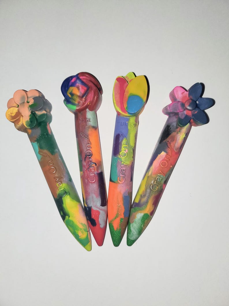May include: Four colorful crayons shaped like flowers. The crayons are labeled "Crayon On!" and feature a variety of colors and designs.