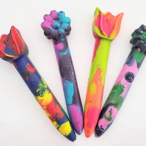 May include: Four colorful crayons shaped like flowers and tulips. The crayons are made by Crayola and have a multi-colored swirl design.