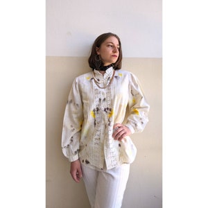 May include: A white button-up shirt with a lace overlay and yellow and brown tie-dye pattern. The shirt has a high collar and long sleeves.