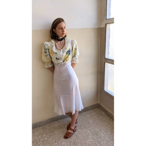 May include: A white dress with a floral print top and a white skirt. The dress has a lace trim and a fitted bodice. The model is wearing a black choker necklace and a pearl necklace.