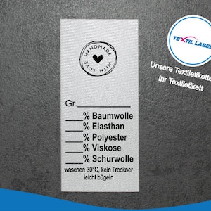 Könnte beinhalten: Ein weißes Stofflabel mit schwarzem Text und einem kleinen schwarzen Herz in einem Kreis. Der Text lautet "Handmade with Love" und "Gr.", gefolgt von einer Liste von Prozentangaben für verschiedene Stoffarten: Baumwolle, Elasthan, Polyester, Viskose und Schurwolle. Das Etikett enthält auch Waschanweisungen: "waschen 30°C, kein Trockner, leicht bügeln".