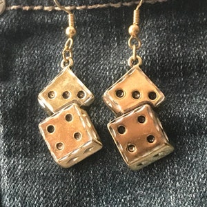 May include: Gold tone dangle earrings featuring two stacked dice charms.