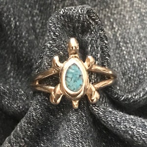May include: A gold ring with a turquoise stone set in a turtle design.