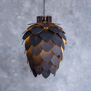 Op de afbeelding: Een donkerhouten hanglamp in de vorm van een dennenappel met een warm licht dat door de houten latten schijnt.