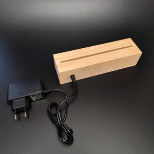 Könnte beinhalten: Ein Holzdisplay mit integriertem LED-Lichtstreifen. Der Ständer ist mit einem schwarzen Netzteil und einem Kabel verbunden.