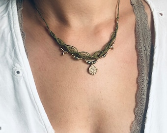 May include: A green and gold necklace with a pendant featuring a geometric design. The necklace is made of macrame and beads.