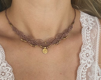 May include: A delicate brown choker necklace with a gold pendant. The necklace is made of braided cord and features small gold beads.