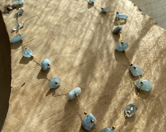 May include: A delicate gold chain necklace with light blue aquamarine stones. The stones are irregular in shape and size, giving the necklace a unique and natural look.