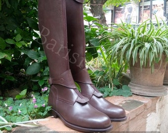 May include: A pair of brown leather riding boots with a zipper on the inside of each boot. The boots have a buckle strap at the top of the shaft and a strap with a buckle around the ankle.