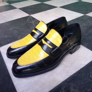 May include: A pair of black leather loafers with yellow crocodile-embossed leather accents. The loafers have a classic penny loafer design with a single strap across the vamp.